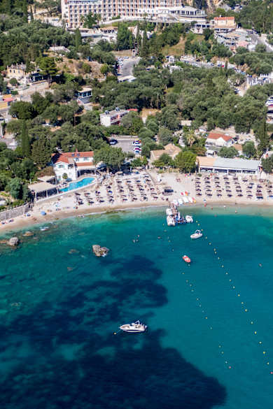 Blick auf einen Strand an türkisem Wasser mit Bäumen und Häusern im Hintergrund